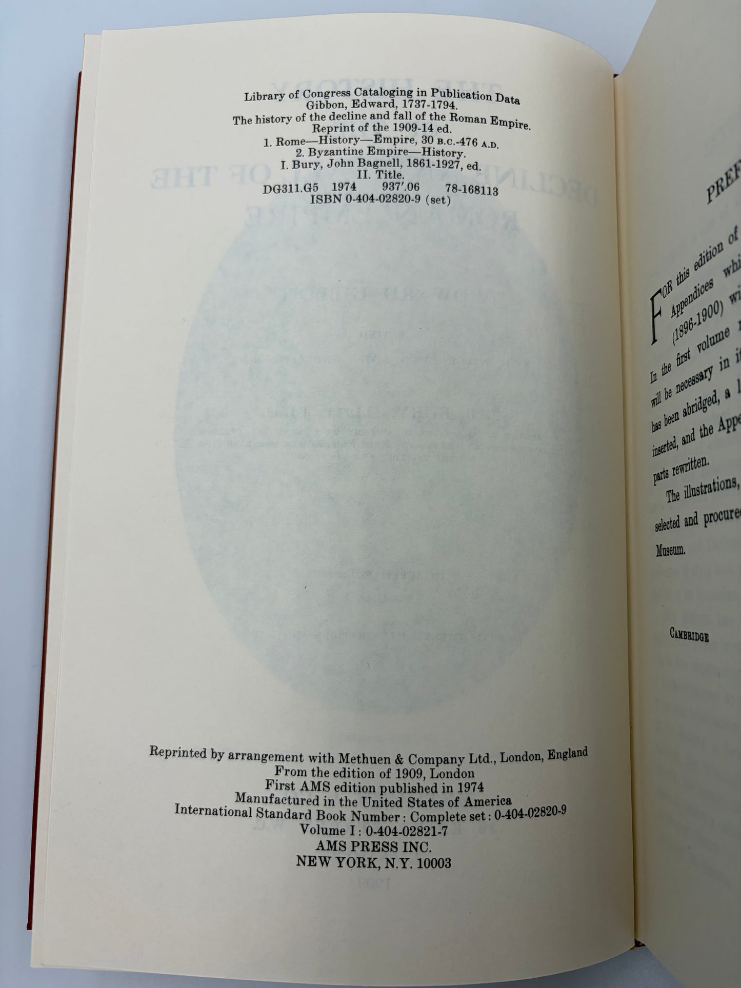 An open book showing the title and copyright page in English from the book ‘The history of the decline and fall of the Roman Empire’ by Edward Gibbon, with a large faded circular watermark across the center. The pages are off-white/cream with black text, and the book is photographed against a light neutral background.