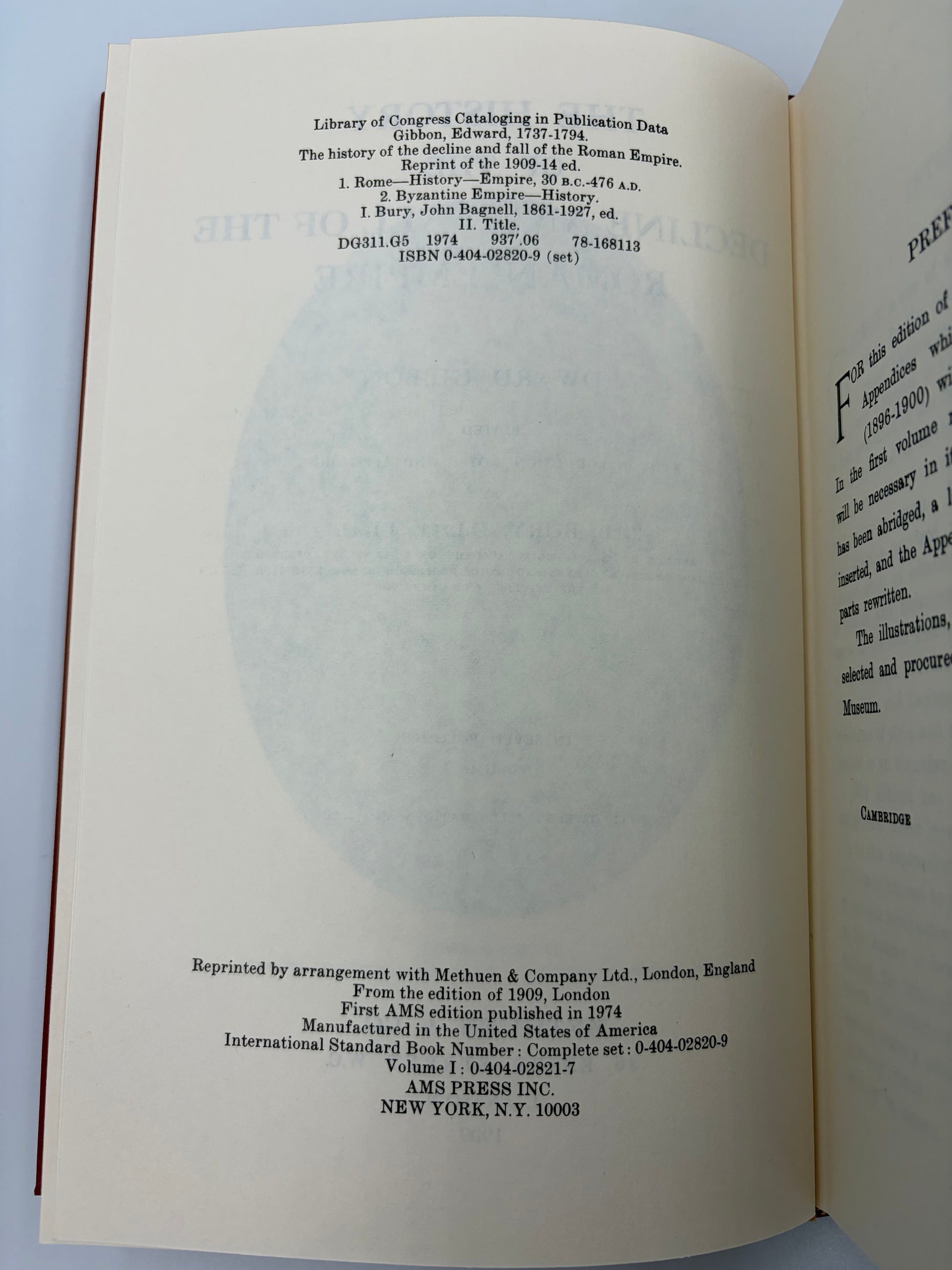 An open book showing the title and copyright page in English from the book ‘The history of the decline and fall of the Roman Empire’ by Edward Gibbon, with a large faded circular watermark across the center. The pages are off-white/cream with black text, and the book is photographed against a light neutral background.