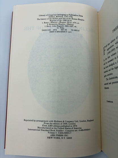 An open book showing the title and copyright page in English from the book ‘The history of the decline and fall of the Roman Empire’ by Edward Gibbon, with a large faded circular watermark across the center. The pages are off-white/cream with black text, and the book is photographed against a light neutral background.