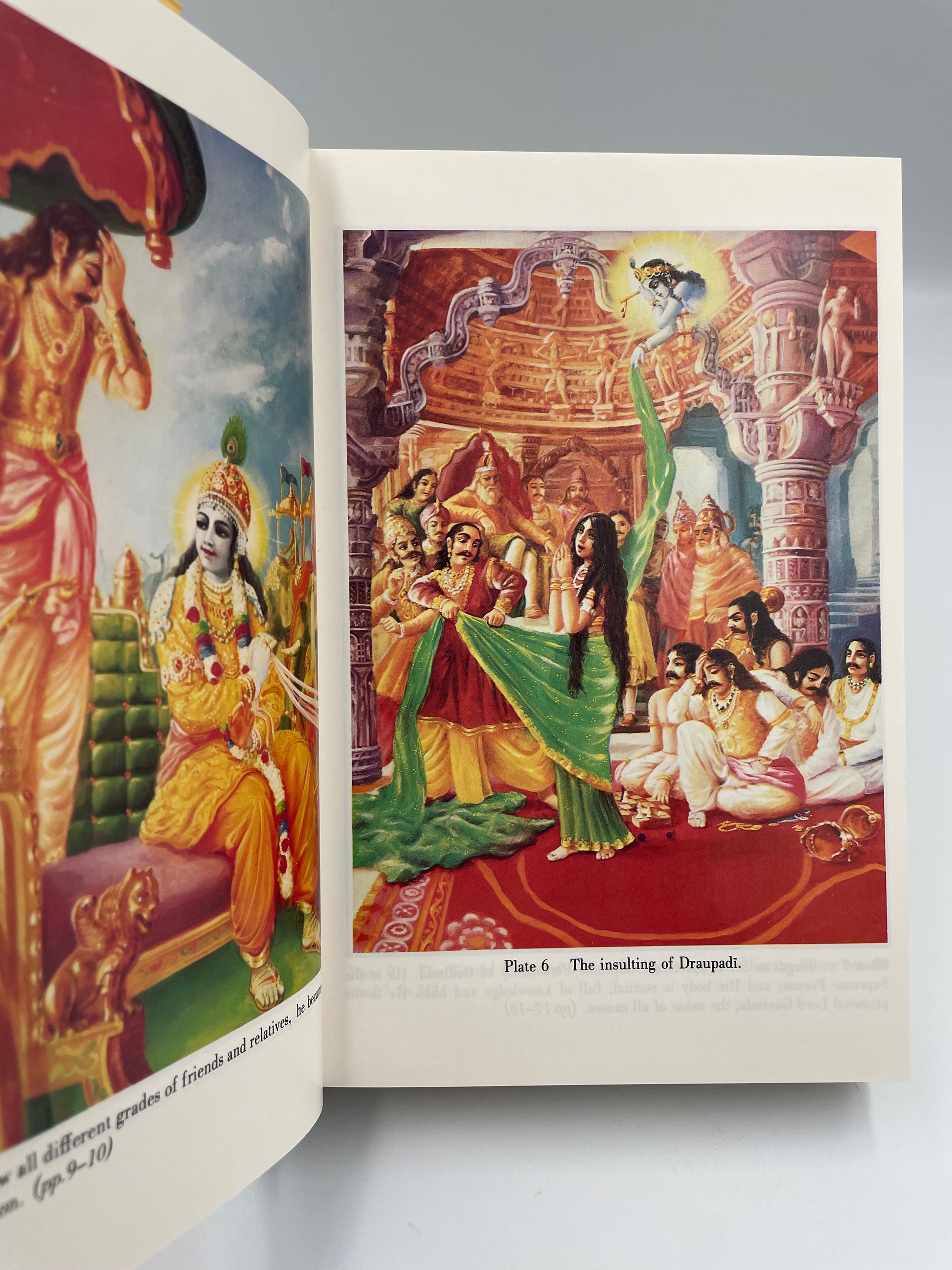 Open book with colorful illustrations of characters in traditional attire on a plain background from ‘Bhagavad-Gita As It Is’.